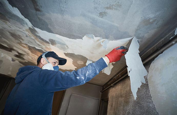 Expert wearing a protective mask and gloves scraping damaged ceiling